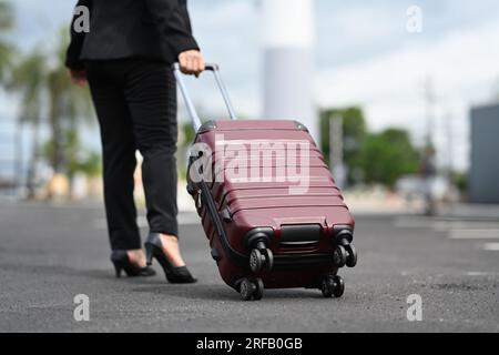Disparo recortado de mujer irreconocible caminando cerca del aeropuerto con una maleta. Concepto de viaje de negocios Foto de stock
