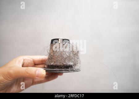 Filtro de papel sucio de un aspirador de mano. Un hombre sostiene un filtro de cono con el polvo y el pelo en un cubo Foto de stock
