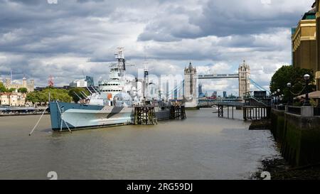 Londres, Reino Unido - 29 de julio de 2023; HMS Belfast y Tower Bridge atracciones turísticas a lo largo de la orilla sur del río Támesis bajo el cielo de mal humor Foto de stock