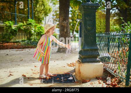 Adorable niña jugando con agua en un día caluroso de verano. Niño feliz caminando en el parque. Actividades al aire libre para niños Foto de stock