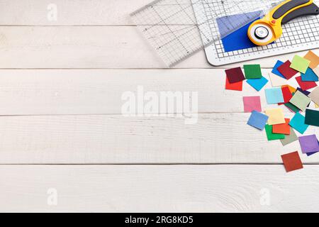 Montón de piezas cuadradas de telas de colores en la superficie de madera blanca, accesorios de acolchado, espacio para el texto Foto de stock