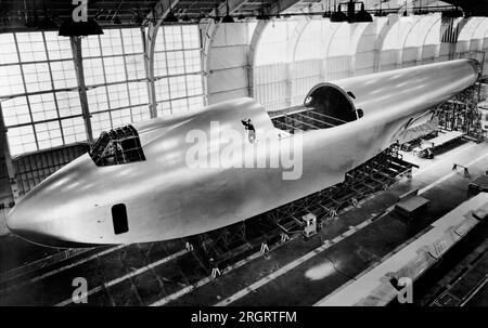 Culver City, California: c. 1946 El casco de 220 pies de largo del barco volador de Howard Hughes en construcción en su hangar. Está a punto de terminar con su capa final de laca de aluminio. La sección cortada es donde las alas encajarán entre sí. Foto de stock