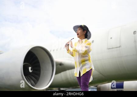 Mujer feliz de los sesenta en ropa de verano y gafas de sol caminando en la pista cerca del avión. Concepto de viaje y vacaciones de verano Foto de stock