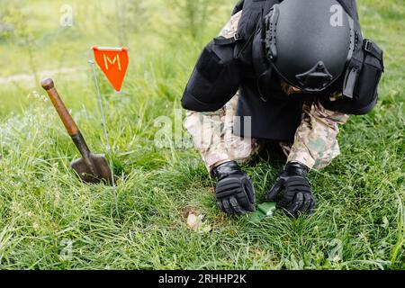 Un hombre con uniforme militar y chaleco antibalas trabaja en el bosque  para desminar el territorio