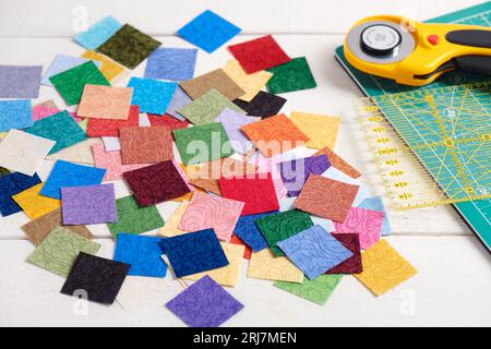 Pila piezas cuadradas de telas coloridas en la superficie de madera blanca, accesorios de acolchado Foto de stock