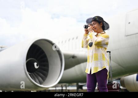 Mujer feliz de los años sesenta en ropa de verano tomando la foto con la cámara cerca del concepto del aeroplano. Viaje y vacaciones de verano Foto de stock