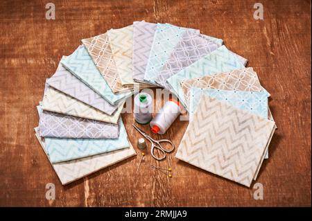 Conjunto de telas pastel dispuestas en círculo y herramientas de costura en el centro sobre fondo de madera Foto de stock