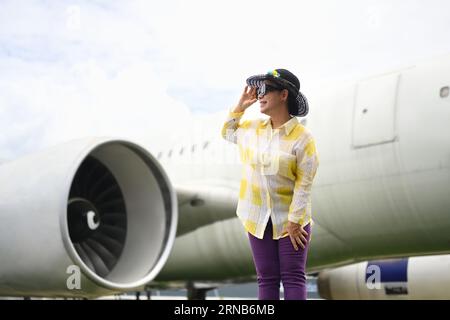Mujer activa de los sesenta en ropa de verano y gafas de sol caminando en la pista cerca del avión. Concepto de viaje y vacaciones de verano Foto de stock