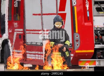 bombero con casco y uniforme a prueba de fuego apaga el fuego y el camión de bomberos en el fondo Foto de stock