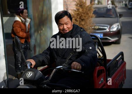 210214 -- YINCHUAN, 14 de febrero de 2021 -- Zhang Junming va de compras en un triciclo electrónico en un mercado cerca de su nueva residencia en el sitio de reubicación de Binhe Jiayuan un día antes del Año Nuevo Lunar Chino en Yinchuan, Región Autónoma de Ningxia Hui en el noroeste de China, 11 de febrero de 2021. Zhang Junming, de 55 años, vivió una vez en el municipio de Hongbaiyang, un remanso económico en el sur de Ningxia. Cuando era joven, Zhang había resultado gravemente herido en un accidente, y por lo tanto sufrió de discapacidades en las piernas que le impidieron buscar oportunidades de trabajo en las grandes ciudades. Así que él y su familia tuvieron que ganarse la vida Foto de stock