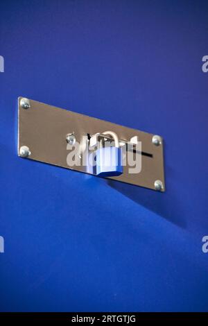 Un candado azul cerrado en una barrera metálica en un almacén Foto de stock