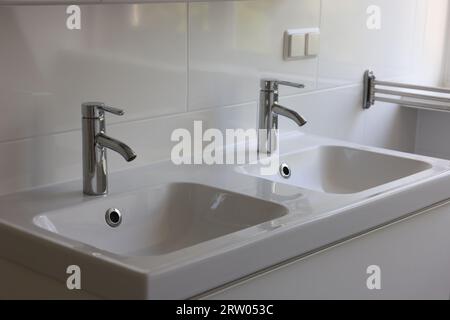 Lavabos blancos limpios con grifos de agua en el baño Foto de stock