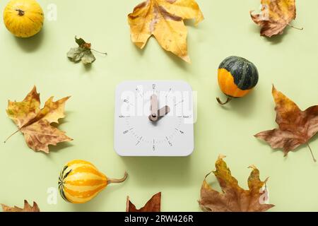 Despertador con hojas de otoño y calabazas sobre fondo verde Foto de stock