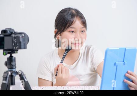 Concepto de blogger de niña de belleza, mujer asiática usa pincel de maquillaje y revisión en transmisión en vivo aislado sobre fondo blanco Foto de stock
