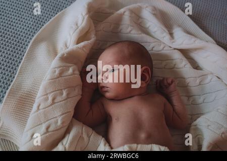 Bebé en una manta blanca bebé acostado en una manta de muselina blanca en  el suelo mirando a la cámara