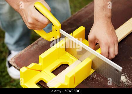 Hombre cortando un listón de madera usando una sierra y una caja de ingletes al aire libre Foto de stock