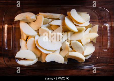 Manzanas peladas y rodajas en un plato de horno de vidrio transparente sobre una mesa de madera Foto de stock
