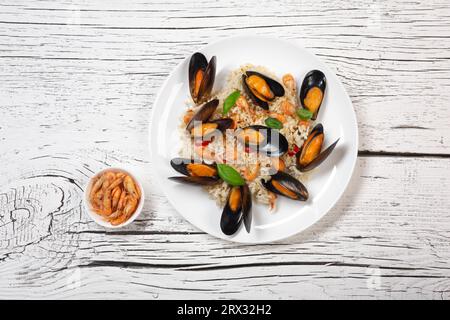 Arroz frito con mejillones de mariscos, camarones y albahaca en un plato sobre mesa de madera agrietada blanca. Vista superior. Foto de stock