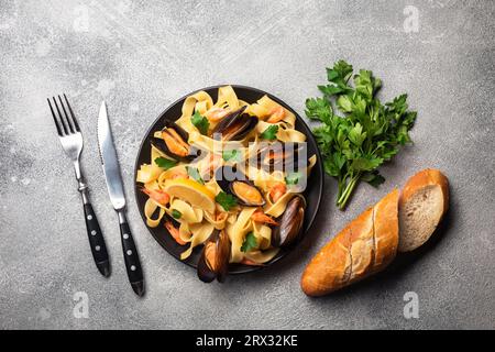 Mejillones con espaguetis, tostadas de pan y perejil en mesa de piedra. Vista superior con espacio de copia Foto de stock