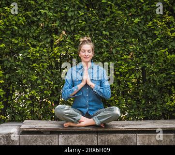 Retrato de mujer meditando en el banco delante del seto Foto de stock