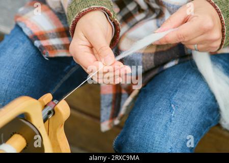 La mujer está hilando lana en una rueda de madera. Primer plano de las manos de una mujer tejiendo lana Foto de stock