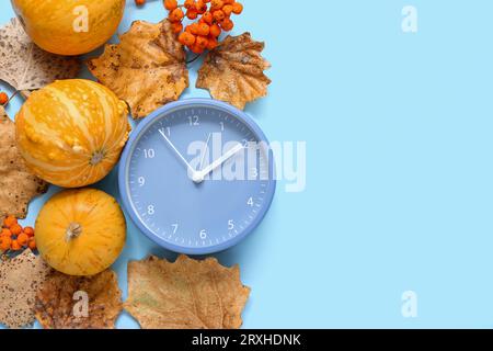 Despertador con hojas de otoño y calabazas sobre fondo azul Foto de stock