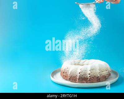 La mano femenina rocía azúcar glaseado en la torta de la tajada Foto de stock
