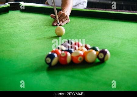 Mano del hombre y brazo Cue jugando juego de billar o preparándose con el objetivo de disparar bolas de billar en una mesa de billar verde. Snooker colorido Foto de stock