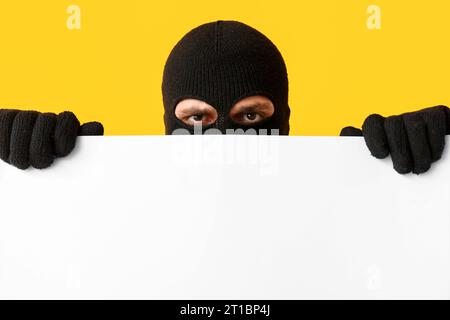 Ladrón masculino con cartel en blanco sobre fondo amarillo Foto de stock