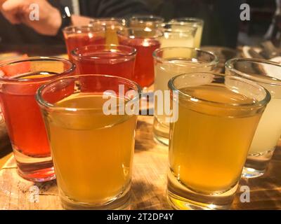 Un conjunto de un montón de deliciosos vasos de color rojo naranja amarillo, tiros con alcohol fuerte, vodka, relleno, brandy en soportes de madera en una mesa en un café, bar, re Foto de stock