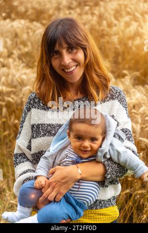 Una joven madre sonriente con su bebé en un campo de paja amarilla en la Bretaña francesa en el verano de julio, cerca del bosque de Broceliande. Francia Foto de stock