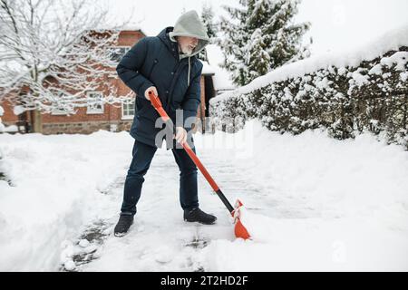 Hombre maduro que palea la nieve en un patio trasero en el día de invierno. Tareas de invierno. Foto de stock