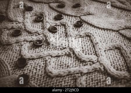 Hermosa textura de un suéter natural cálido suave con un patrón de punto de hilo y pequeños botones redondos en blanco y negro. El fondo. Foto de stock