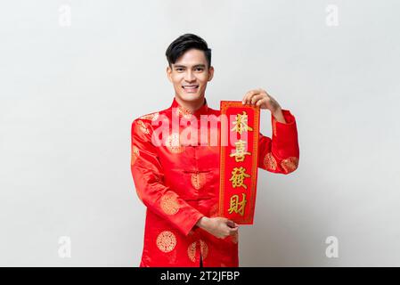 Hombre asiático sonriente guapo que muestra el pergamino rojo en fondo gris claro de estudio aislado para conceptos de año nuevo chino, texto extranjero significa que puede atta Foto de stock