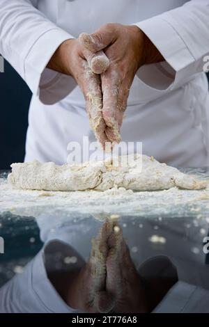 Cerca de un chef frotando sus manos sobre una masa en una mesa de vidrio Foto de stock