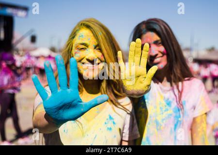 Cierre dos mujeres jóvenes mostrando sus manos pintadas con color holi Foto de stock