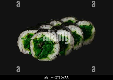 rollo de sushi con ensalada de chuka aislado sobre fondo negro. Foto de stock