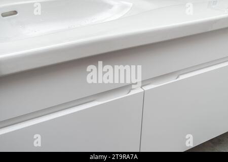 Mueble de tocador de baño montado en la pared con doble lavabo de porcelana blanca y grifo sensor de plata en baño moderno con hormigón y azulejos de madera de cerca Foto de stock