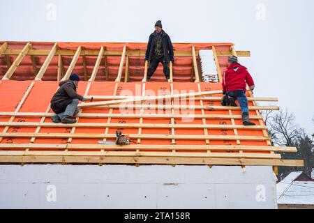 Irpin - Ucrania, marzo - 13, 2021: Contratistas de techado que instalan tablas de techo y barreras de vapor para baldosas de metal en invierno. Foto de stock