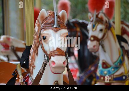 Cabezas de caballos pintados en un carrusel o carrusel en una feria divertida en Perth, Australia Occidental, tienen plumas rojas brillantes Foto de stock