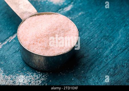 Sal rosa del Himalaya en cuchara de medición sobre fondo de madera. Foto de stock