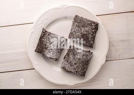 Tres piezas de brownie de chocolate clásico con plato de cerámica en mesa de madera, macro, vista superior. Foto de stock