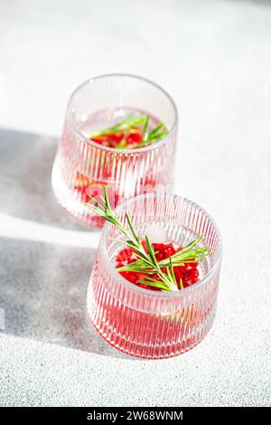 Desde arriba de cócteles gin tonic iluminados por el sol con granada y romero en vasos texturizados en una superficie brillante Foto de stock
