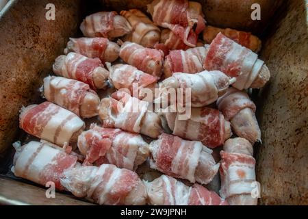 Salchichas de chipolata envueltas en tocino o 'cerdos en mantas' en una bandeja para hornear listo para cocinar en un horno. Foto de stock