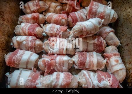 Salchichas de chipolata envueltas en tocino o 'cerdos en mantas' en una bandeja para hornear listo para cocinar en un horno. Foto de stock