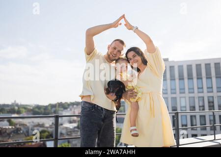 Familia con las manos levantadas en forma de casa en la azotea de la ciudad Foto de stock