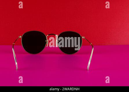 Gafas de sol clásicas con marco de metal sobre un fondo rojo y base rosa Foto de stock
