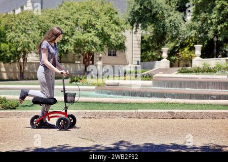 Mujer joven utiliza Scooter para ayudar a moverse con la pierna rota Foto de stock