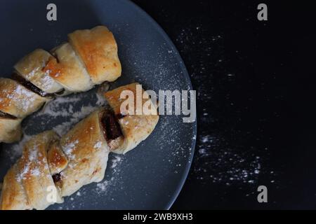 Ausencias horneadas en la masa en un plato blanco contra fondo negro. Bollos de pastelería de salchichas Puff. Foto de stock