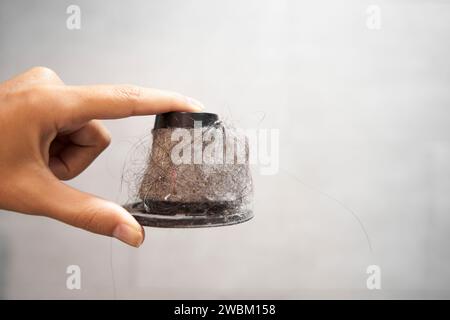 Filtro de papel sucio de un aspirador de mano. Un hombre sostiene un filtro de cono con el polvo y el pelo en un cubo Foto de stock